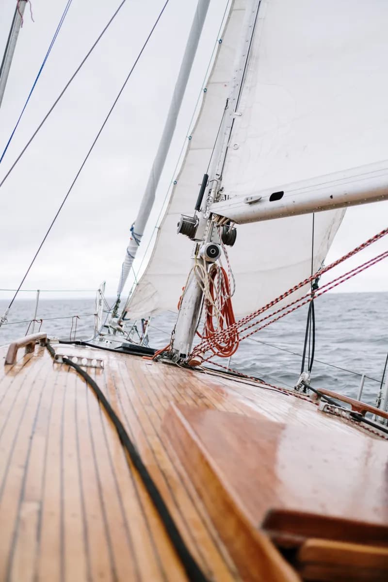 Immagine di esempio BookNoFees: ponte in legno di una barca a vela con cime e vela bianca