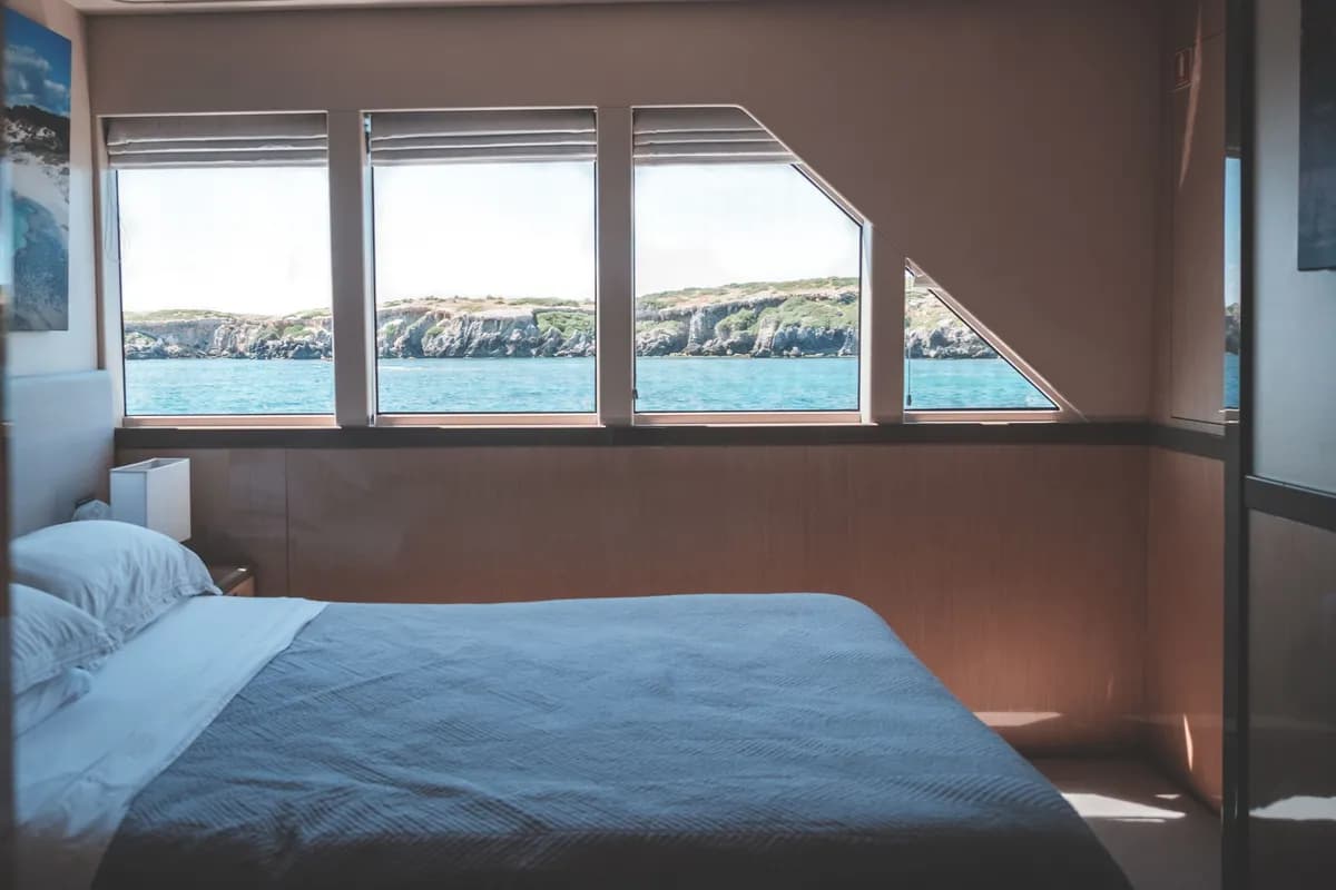 Immagine di esempio BookNoFees: cabina luminosa di una barca con letto e ampie finestre affacciate sul mare