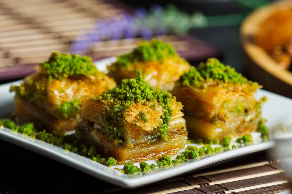 BookNoFees: Foto di esempio: Quattro pezzi di baklava a strati guarniti con pistacchi tritati su un piatto bianco