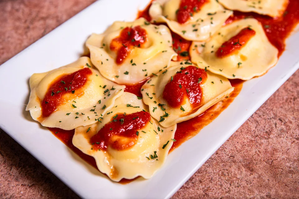 BookNoFees: Foto di esempio: Ravioli conditi con salsa di pomodoro ed erbe aromatiche su un piatto bianco