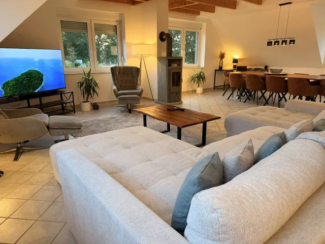 BookNoFees: casa vacanza a Stuhr – Soggiorno con divano a L, stufa a legna e zona pranzo con tavolo in legno