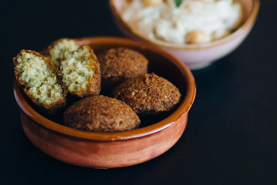 BookNoFees: Foto di esempio: Polpette di falafel, tra cui una tagliata a metà, in una ciotola con l'hummus sullo sfondo