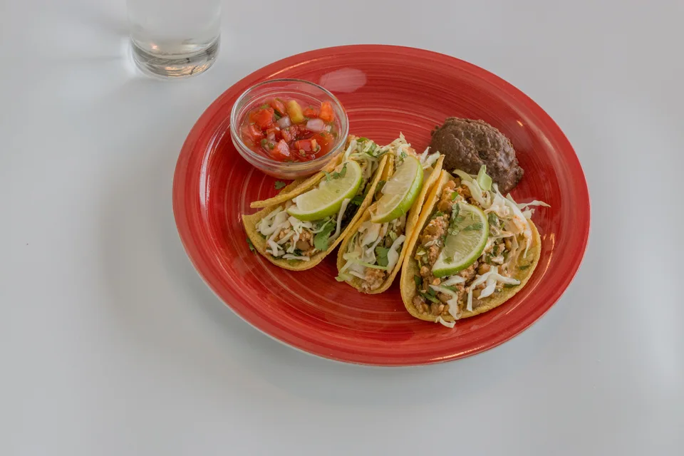 BookNoFees: Foto di esempio: Tre tacos guarniti con fette di lime e salsa su un piatto rosso