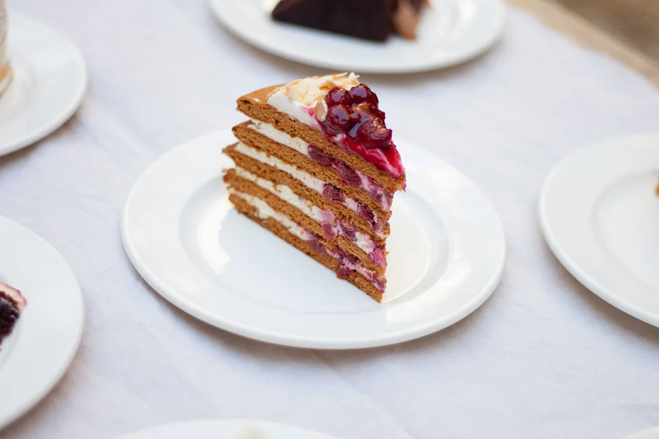BookNoFees: Foto di esempio: Una fetta di torta a strati guarnita con frutti di bosco su un piatto bianco
