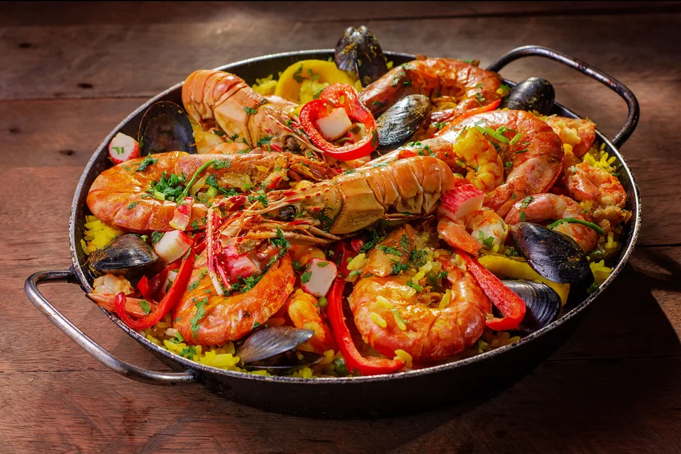 BookNoFees: Foto di esempio: Una padella di paella ai frutti di mare guarnita con crostacei e peperoni rossi